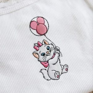 Puede incluir: Tejido blanco acanalado con un dise&ntilde;o bordado de un gatito blanco sosteniendo un globo rosa. El gatito tiene un lazo rosa, un collar y un globo. El globo tiene forma de Mickey Mouse rosa.