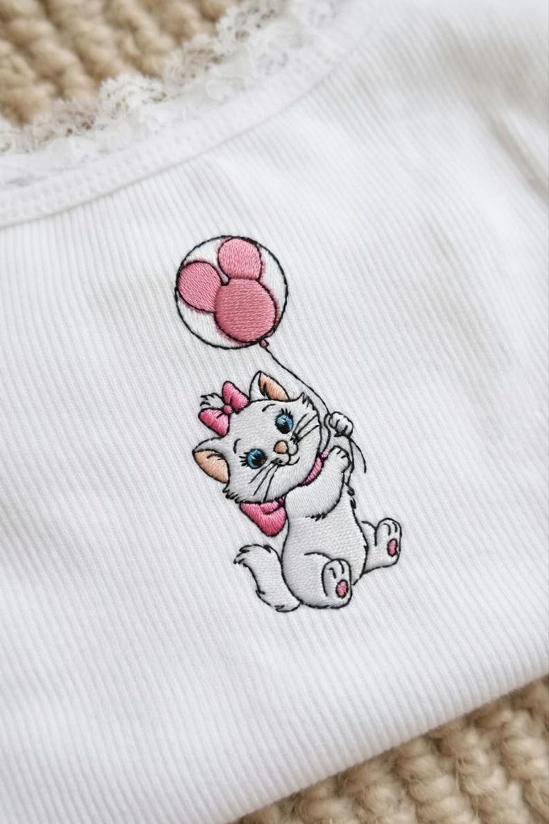 Puede incluir: Tejido blanco acanalado con un dise&ntilde;o bordado de un gatito blanco sosteniendo un globo rosa. El gatito tiene un lazo rosa, un collar y un globo. El globo tiene forma de Mickey Mouse rosa.