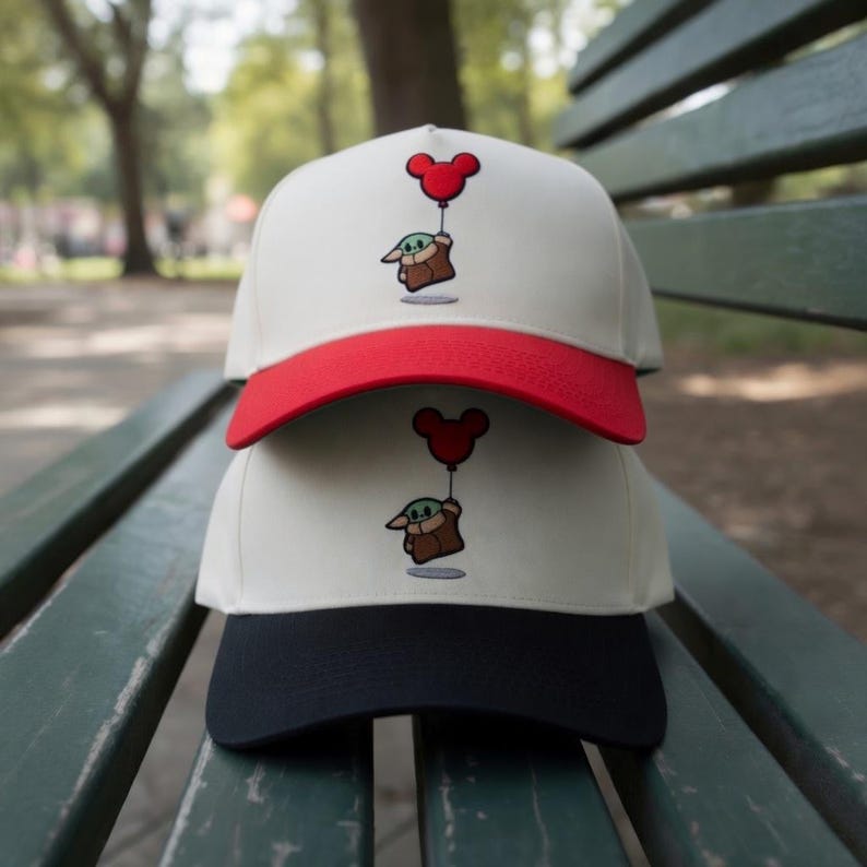 May include: Two baseball caps stacked on top of each other. The top cap has a white crown and red brim, with an embroidered image of a cartoon character holding a Mickey Mouse balloon. The bottom cap has a white crown and a black brim.