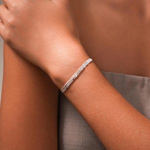 May include: A slender silver-toned bracelet featuring a delicate, multi-strand chain design. The piece consists of several thin, interconnected metallic links that wrap around the wrist, creating a refined and polished appearance with a subtle shine.