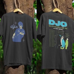 Könnte beinhalten: Schwarzes T-Shirt mit einer blauen Grafik eines Musikers und dem Wort "djo". Auf der Rückseite des Shirts steht "DJO BACK ON YOU WORLD TOUR 2025" mit Tourdaten und einer Grafik von drei Figuren.