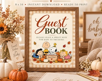 Op de afbeelding: Een printbaar gastenboekbord in een houten lijst met de tekst Guest BOOK en Please leave a sweet note for baby to treasure, geïllustreerd met Snoopy en vrienden omringd door herfstbladeren en pompoenen, 20 x 25 cm.