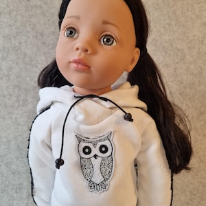 Peut inclure: Poupée aux cheveux noirs et aux yeux gris, vêtue d'un sweat à capuche blanc orné d'un motif de hibou noir et blanc. Le sweat à capuche a un cordon de serrage et une bordure noire. La poupée porte un pantalon blanc assorti avec une bordure noire.