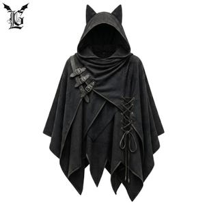 May include: Black hooded cape with cat ears, leather straps, and buckles. The cape features a unique asymmetrical design with a lace-up detail on the side. The gothic-inspired outerwear is made of a textured fabric.