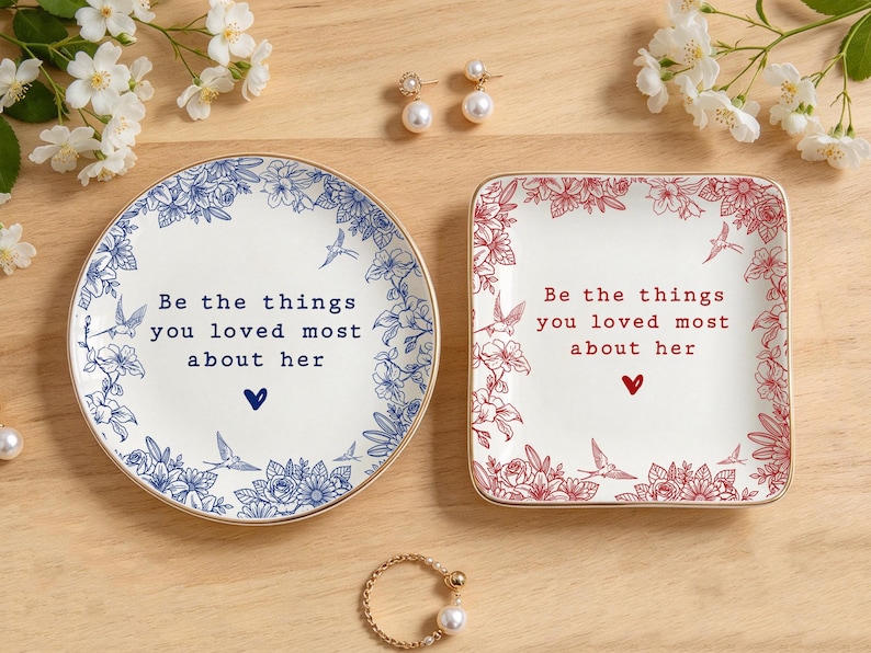 Może przedstawiać: Okrągła ceramiczna miseczka i kwadratowa ceramiczna miseczka, obie ze złotym brzegiem, kwiatowymi obw&oacute;dkami i napisem "Be the things you loved most about her" oraz małą ikoną serca. Okrągła miseczka ma niebieskie detale, a kwadratowa czerwone.