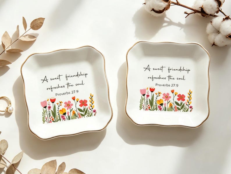 May include: Two square white ceramic trinket dishes with scalloped edges and gold-toned rims. Each dish features a colorful floral illustration at the bottom and the black text: A sweet friendship refreshes the soul. Proverbs 27:9.