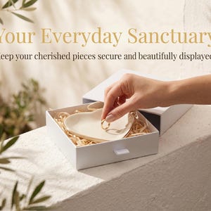 May include: A white jewelry box with a heart-shaped dish inside, filled with straw-like material. A hand places a gold ring in the dish. The text "Your Everyday Sanctuary" is at the top.