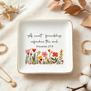 May include: A square white ceramic trinket dish with a gold-toned rim. The center features the black text A sweet friendship refreshes the soul Proverbs 27:9 above a colorful illustration of various wildflowers in shades of pink, red, and yellow.