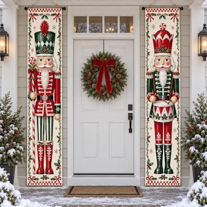 May include: Two vertical rectangular banners featuring nutcracker figures. The left banner shows a nutcracker holding a candy cane staff. The right banner shows a nutcracker playing a drum. Both feature red, green, and white holiday motifs.