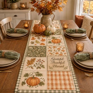 May include: A rectangular fabric table runner featuring a patchwork design with autumn motifs including orange pumpkins, fall leaves, berries, and a plaid pattern. The center square displays the text Grateful Thankful Blessed in brown script.