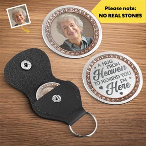 May include: A black leather keychain with a silver ring, holding a round photo pendant. Two additional round pendants are visible, one with a photo and the other with the text "A HUG FROM Heaven to remind you I'm Here".