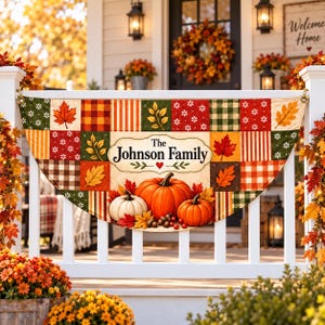 May include: A semi-circular fabric banner featuring a patchwork design of autumn leaves, plaid patterns, and floral motifs. The center displays the text The Johnson Family above a cluster of orange and white pumpkins, acorns, and red berries.