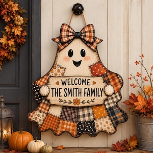 Peut inclure: Une décoration murale en forme de fantôme avec un motif patchwork orange, noir et blanc. Un nœud est placé en haut et un panneau central indique WELCOME THE SMITH FAMILY avec des cœurs et des fleurs. Le design inclut des yeux et une bouche noirs.