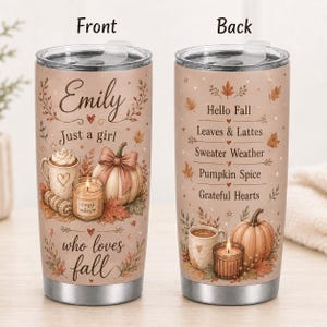 May include: Two stainless steel tumblers with clear lids featuring autumn-themed graphics. The front displays the text Emily Just a girl who loves fall with a mug, candle, and pumpkin. The back lists Hello Fall, Leaves & Lattes, Sweater Weather, Pumpkin Spice, Grateful Hearts.