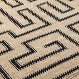 Peut inclure: Un tapis rectangulaire présentant une base texturée beige avec un motif géométrique noir audacieux en forme de clé grecque. Le design se compose de lignes angulaires interconnectées formant un motif répétitif en labyrinthe avec des franges.