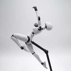 May include: A white and black articulated action figure in a dynamic pose, supported by a black stand. The figure has a rounded head and is designed to be poseable. The joints and key areas are black, contrasting with the speckled white body. The figure is designed for display.