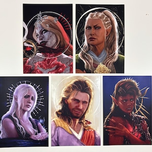 May include: Five fantasy art prints featuring portraits of characters with detailed facial features and ethereal halos. The characters have varied skin tones, hair colors, and expressions. The prints are on a white surface with a black background.