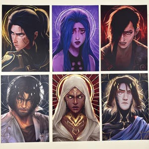 May include: Six art prints featuring stylized portraits of characters with detailed facial expressions and dramatic lighting. Each portrait has a unique color palette, with hues of blue, purple, gold, and red. The prints have a fantasy theme.