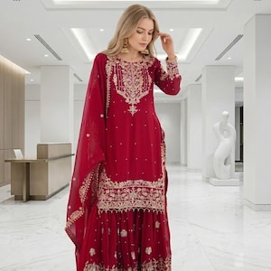 Puede incluir: Un traje Sharara rojo con bordados dorados. La parte superior de manga larga y los pantalones de pernera ancha est&aacute;n adornados con intrincados dise&ntilde;os dorados. Una dupatta roja a juego completa el conjunto. Adecuado para ocasiones especiales.
