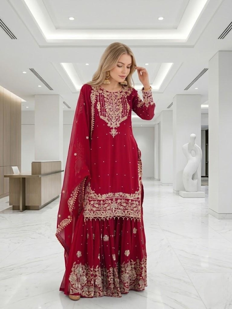 Puede incluir: Un traje Sharara rojo con bordados dorados. La parte superior de manga larga y los pantalones de pernera ancha est&aacute;n adornados con intrincados dise&ntilde;os dorados. Una dupatta roja a juego completa el conjunto. Adecuado para ocasiones especiales.