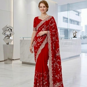 May include: A striking red saree, adorned with elaborate gold embroidery and a scalloped edge. This traditional Indian garment showcases detailed floral designs and is paired with a matching blouse. The saree is a formal wear item.