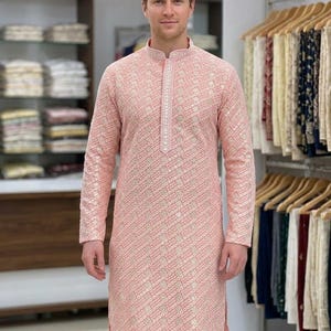 May include: A peach-colored long-sleeve kurta featuring a mandarin collar and a vertical placket with intricate white embroidery. The fabric is covered in a repeating geometric pattern of small white squares and dots throughout the entire garment.