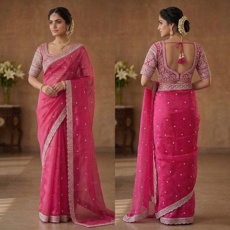 Op de afbeelding: Een felroze sari met ingewikkelde zilveren borduursels langs de randen en verspreide witte stippen. De bijpassende blouse heeft gedetailleerde borduursels op de mouwen en halslijn. De sari is elegant gedrapeerd en toont de vloeiende stof.
