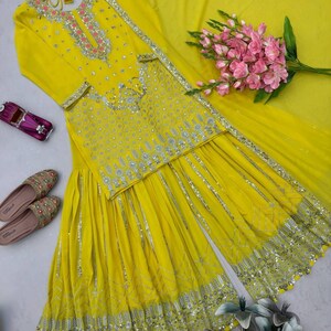 Pu&ograve; includere: Un completo salwar kameez giallo brillante con intricati abbellimenti argentati. L'ensemble include una tunica a maniche lunghe, pantaloni a gamba larga e una sciarpa abbinata. Accenti floreali rosa e un paio di scarpe decorate completano il look. &Egrave; presente anche una piccola macchina giocattolo.