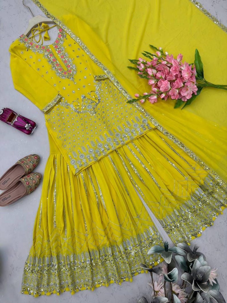 Pu&ograve; includere: Un completo salwar kameez giallo brillante con intricati abbellimenti argentati. L'ensemble include una tunica a maniche lunghe, pantaloni a gamba larga e una sciarpa abbinata. Accenti floreali rosa e un paio di scarpe decorate completano il look. &Egrave; presente anche una piccola macchina giocattolo.