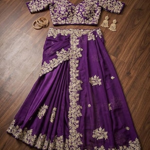 May include: A deep purple ensemble featuring a short-sleeved blouse and a long skirt, both adorned with intricate gold floral embroidery. The set includes a pair of matching gold drop earrings and three thin gold bangles, all displayed together.
