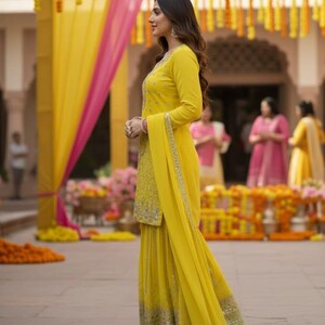 Pu&ograve; includere: Una donna in un salwar kameez giallo ricamato con un dupatta abbinato. L'outfit ha abbellimenti argentati e viene indossato con sandali dorati. Lo sfondo presenta decorazioni gialle e rosa, suggerendo un'occasione festosa.