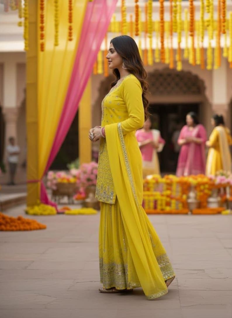 Pu&ograve; includere: Una donna in un salwar kameez giallo ricamato con un dupatta abbinato. L'outfit ha abbellimenti argentati e viene indossato con sandali dorati. Lo sfondo presenta decorazioni gialle e rosa, suggerendo un'occasione festosa.