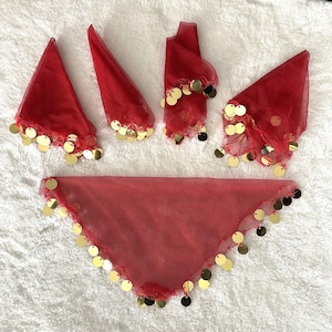 Puede incluir: Un conjunto de piezas de vestuario de danza rojas, que incluyen pañuelos triangulares y brazaletes. Cada pieza está adornada con lentejuelas doradas. La tela es transparente y ligera, adecuada para el movimiento y la actuación.