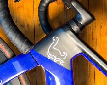 May include: Close-up of a blue and black road bicycle. The frame has a white graphic of a swan on a skateboard. The handlebars are black with black tape. The tires have a red stripe.