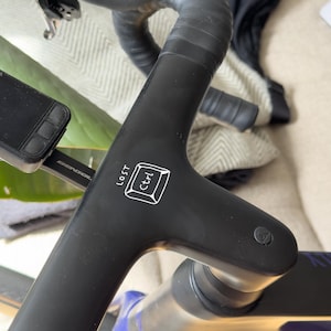 Op de afbeelding: Zwart fietsstuur met een witte "Ctrl"-toetsafbeelding en het woord "LOST" op de stuurpen. Het stuur is omwikkeld met zwart tape. Een smartphone is aan de linkerkant gemonteerd.