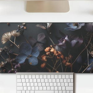 May include: A rectangular desk mat featuring a dark floral design with blue, purple, and orange flowers. The mat is placed on a white desk with a keyboard, mouse, and monitor. The mat has the text "25 HOURS STUDIO".