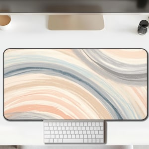 Op de afbeelding: Rechthoekige bureaumat met een aquarelontwerp. De mat heeft een vloeiend patroon van zachte kleuren, waaronder perzik, beige, grijs en blauw. Een wit toetsenbord en muis zijn respectievelijk onder en rechts van de mat geplaatst.