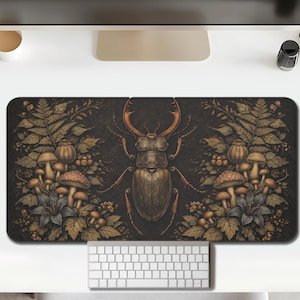 Pode incluir: Tapete de rato retangular com uma ilustração detalhada de um besouro veado com grandes chifres, rodeado por cogumelos, fetos e flores em tons de castanho, verde e bege. O fundo é escuro.
