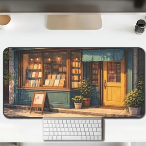 Puede incluir: Alfombrilla de escritorio rectangular con una ilustración de una librería pintoresca. La fachada tiene una puerta amarilla, adornos turquesa y una ventana que muestra libros. Un pequeño letrero está al frente.