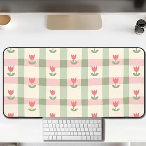 May include: A rectangular desk mat with a repeating pattern of pink tulips and green stems on a cream-colored plaid background. The mat is designed to sit under a keyboard and mouse, providing a decorative and functional workspace.