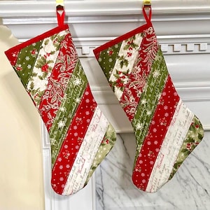 May include: Two Christmas stockings with red, green, and white patterned fabric. The stockings have a diagonal striped design with holly, paisley, and snowflake patterns. The top and hanging loop are red.