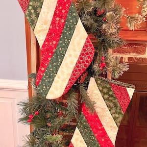 May include: Two Christmas stockings with red, green, and cream-colored diagonal stripes. The stockings are decorated with festive patterns and hang from a wooden structure adorned with greenery and red berries. The stockings are approximately 18 inches long.