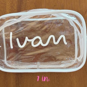 May include: A rectangular clear plastic zippered pouch with white trim. The name "Ivan" is printed in white script on the front. The pouch measures 7 inches in width and 4.12 inches in height as indicated by the text labels on the image.