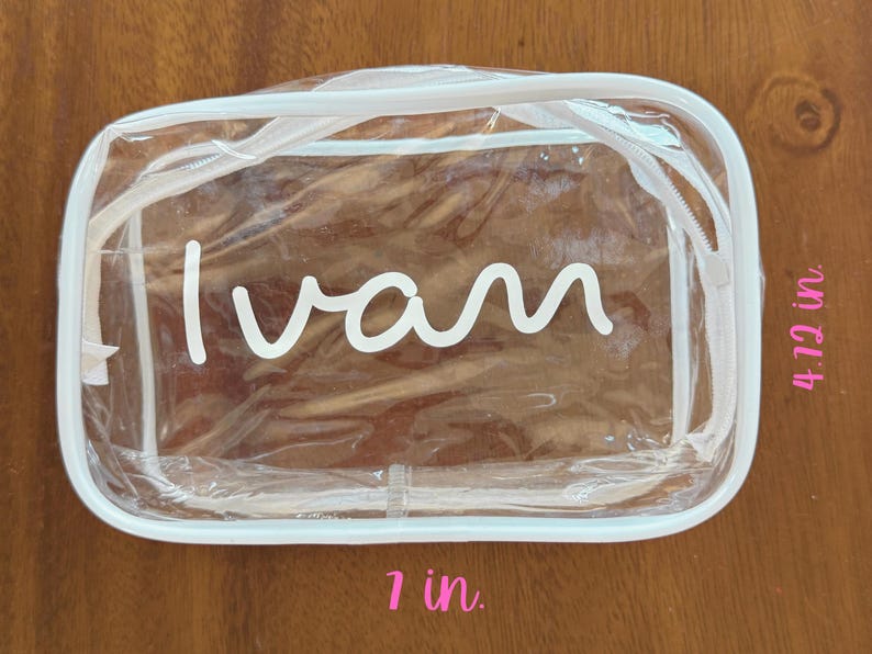 May include: A rectangular clear plastic zippered pouch with white trim. The name "Ivan" is printed in white script on the front. The pouch measures 7 inches in width and 4.12 inches in height as indicated by the text labels on the image.