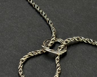 May include: Silver-toned necklace with a twisted rope design. The necklace features a loop and a circular element, all against a dark background. The metal has a slightly aged appearance.