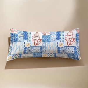 Może przedstawiać: Prostokątna poduszka z patchworkowym wzorem przedstawiającym muszle, ryby i geometryczne wzory w odcieniach niebieskiego, czerwonego i białego. Poduszka ma około 50 cm długości.