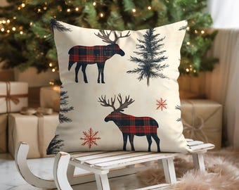 May include: A square cushion with a cream background, patterned with moose silhouettes in red and black plaid, snowflakes, and pine trees. The cushion is displayed on a white wooden sledge.