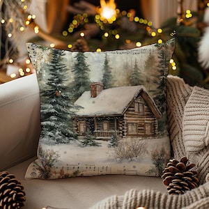 Puede incluir: Cojín decorativo cuadrado con una escena de cabaña de invierno. El cojín muestra una pintura de acuarela de una cabaña cubierta de nieve entre árboles de hoja perenne. Notas musicales impresas en la parte superior e inferior.