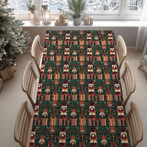 Peut inclure: Une nappe rectangulaire sur le thème de Noël avec un motif répété de casse-noisettes rouges, noirs et dorés sur un fond vert foncé. La nappe est posée sur une table en bois avec quatre chaises.