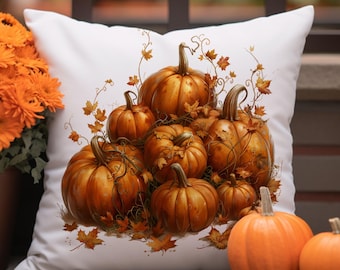 Op de afbeelding: Wit vierkant kussen met een herfstontwerp. Het heeft een cluster van oranje pompoenen met groene stelen en wijnstokken, omringd door herfstbladeren. Twee kleine pompoenen liggen voor het kussen en oranje bloemen staan links.